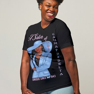 May include: A black t-shirt with a pink and blue graphic of a woman wearing a blue suit and a hat. The text "A Sister of Gamma Phi Delta" and "Unique Since 1943" are printed on the shirt.