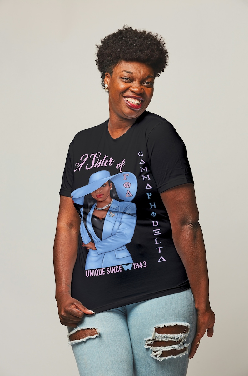 May include: A black t-shirt with a pink and blue graphic of a woman wearing a blue suit and a hat. The text "A Sister of Gamma Phi Delta" and "Unique Since 1943" are printed on the shirt.