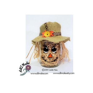 May include: A scarecrow face is painted on a glass jar, decorated with straw, a burlap hat, and a small orange and yellow flower.