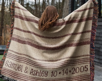 May include: A beige and brown striped blanket with fringed edges. The blanket has the names "Samuel & Ashley" and the date "10.14.2005" printed on it. The blanket is being held up, with the person's back to the camera.