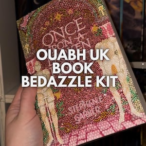 Peut inclure: Une couverture de livre rose et rouge avec un design scintillant. Le titre du livre est "Once Upon a Broken Heart" et l'auteur est Stephanie Garber. La couverture présente deux personnages avec un design rose et blanc. Le texte "OUABH UK BOOK BEDAZZLE KIT" est imprimé sur la couverture.