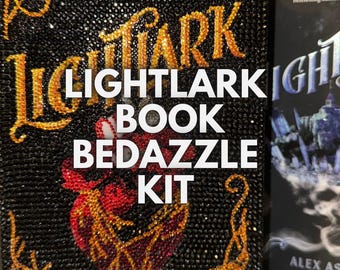 May include: A black book cover with gold and red rhinestones. The book cover has the text "Lightlark Book Bedazzle Kit" on it.