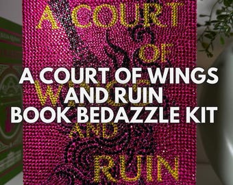 以下が含まれることがあります： ラインストーンがついたピンクと黒のブックカバー。タイトルは「A Court of Wings and Ruin」、著者は「Sarah J. Maas」。これは本のデコレーションキットです。
