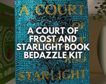 Peut inclure: Une couverture de livre bleue avec des lettres dorées qui disent "A Court of Frost and Starlight Book Bedazzle Kit". La couverture du livre est recouverte de strass.