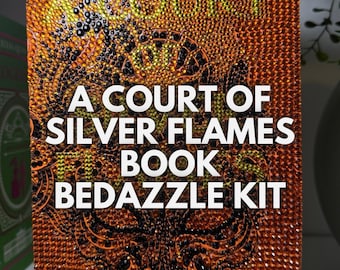 May include: A Court of Silver Flames book bedazzling kit with an orange and black design. The kit features a cover with rhinestones and the title "A Court of Silver Flames Book Bedazzle Kit" and the author's name "Sarah J. Maas".
