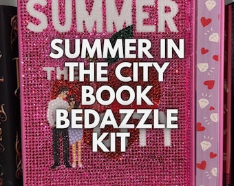 以下が含まれることがあります： キラキラと輝くピンク色の表紙の書籍。表紙には「SUMMER IN THE CITY BOOK BEDAZZLE KIT」という文字と、作者の名前「ALEX ASTER」が書かれています。書籍はラインストーンと赤いリンゴのグラフィックで飾られています。