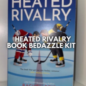 May include: A book cover with the title "HEATED RIVALRY" in white letters on a blue background. The cover features hockey players in action. The text "HEATED RIVALRY BOOK BEDAZZLE KIT" is also visible.