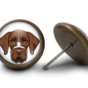 Pode incluir: Brincos de pressão com um desenho de cão castanho e branco sobre fundo branco. Os brincos têm uma moldura de metal cor de bronze e um pino para orelhas furadas.