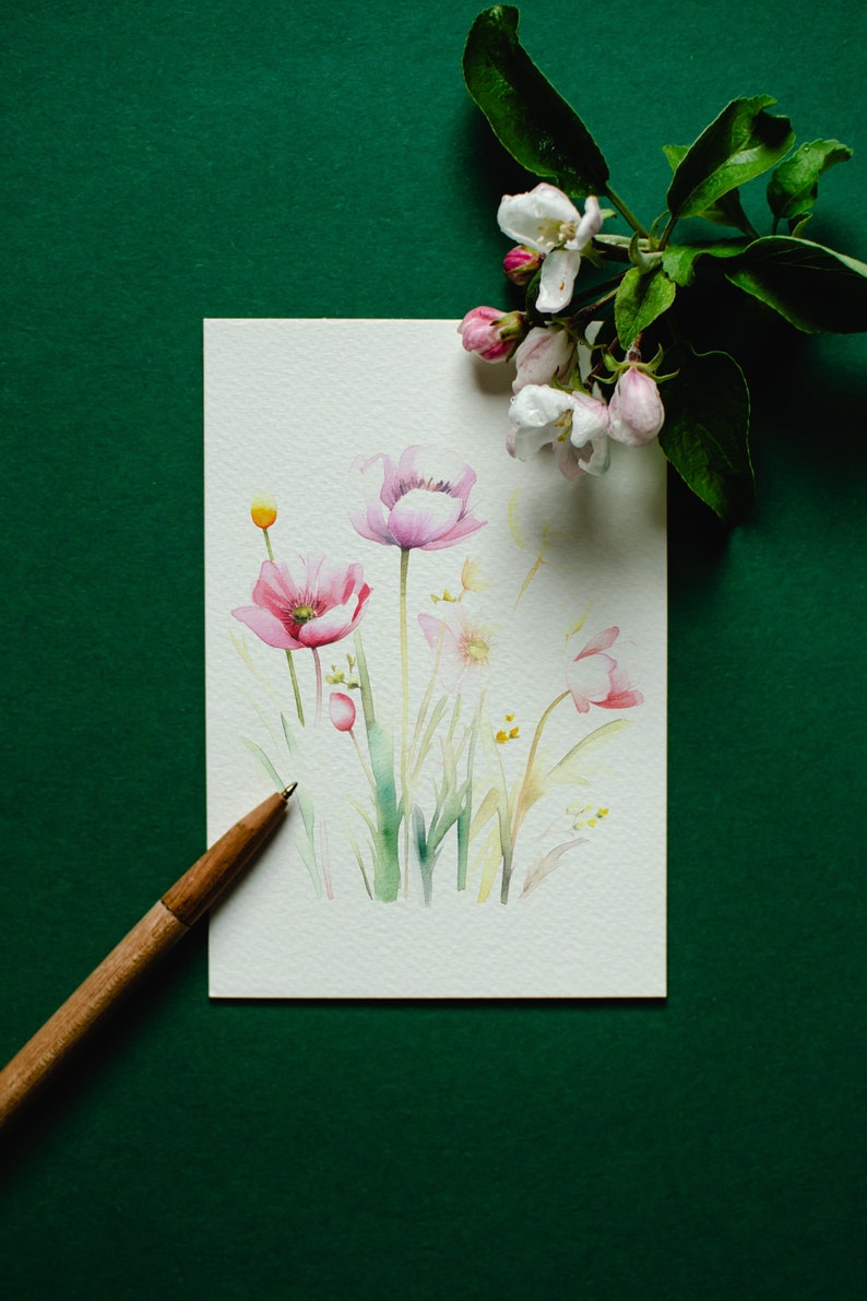 May include: A watercolor painting of pink flowers with green stems and leaves on a white background. The painting is on a green surface with a wooden pencil.