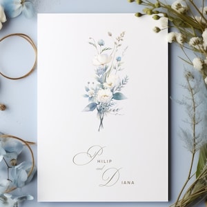 May include: A white card with a watercolour illustration of a bouquet of white flowers with blue accents. The text "Philip and Diana" is printed in gold script at the bottom of the card.