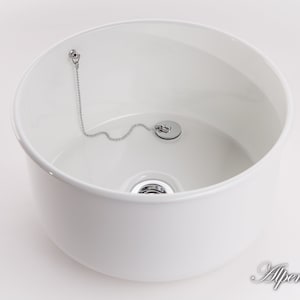 K&ouml;nnte beinhalten: Wei&szlig;e Keramiksp&uuml;le mit einem verchromten Abflussstopfen und einer Kette. Die Sp&uuml;le ist rund und hat eine glatte, gl&auml;nzende Oberfl&auml;che.