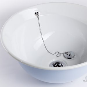 Puede incluir: Un lavabo de cer&aacute;mica blanca con un tap&oacute;n de desag&uuml;e cromado y una cadena. El lavabo est&aacute; vac&iacute;o y listo para usar.