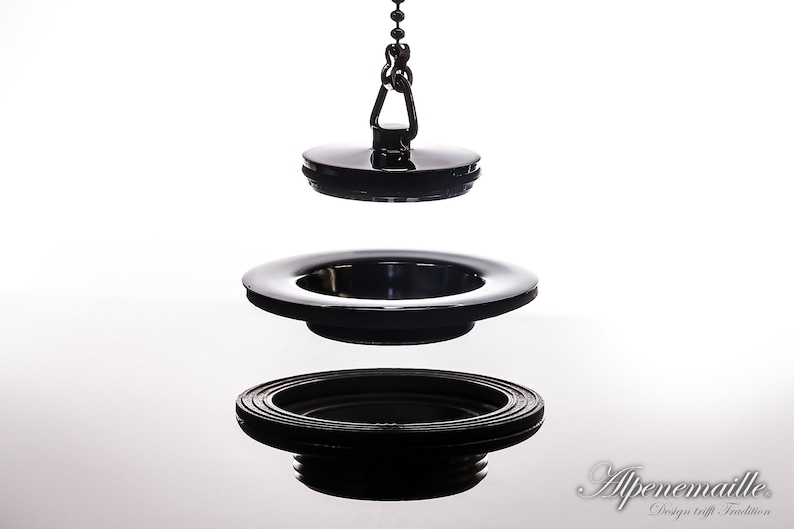 May include: A black sink drain stopper with a chain. The stopper is made of metal and has a round shape. The chain is attached to the stopper and is used to lift the stopper out of the drain.