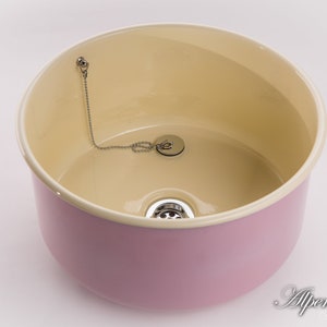 K&ouml;nnte beinhalten: Ein rosa Keramiksp&uuml;le mit cremefarbenem Innenraum. Die Sp&uuml;le hat einen Abfluss mit einer Kette und einem Stopfen.