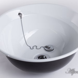 Puede incluir: Un lavabo de cer&aacute;mica blanca con exterior negro. El lavabo tiene un tap&oacute;n de desag&uuml;e cromado con una cadena.