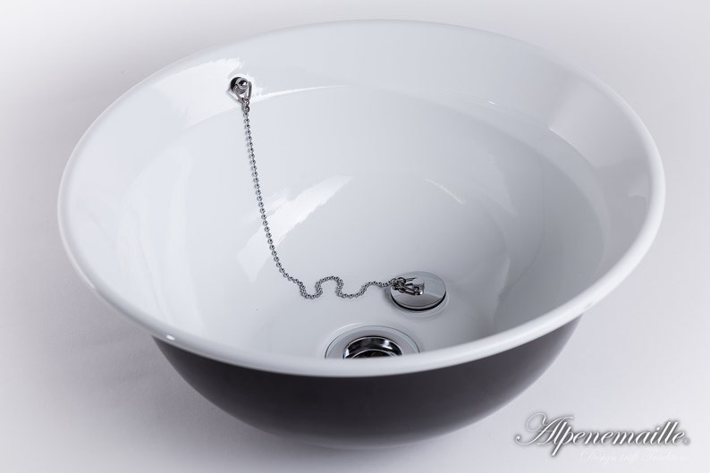 Puede incluir: Un lavabo de cer&aacute;mica blanca con exterior negro. El lavabo tiene un tap&oacute;n de desag&uuml;e cromado con una cadena.