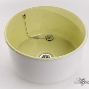 K&ouml;nnte beinhalten: Ein wei&szlig;es Keramikwaschbecken mit gelbem Innenraum. Das Waschbecken hat einen Abflussstopfen mit einer Kette.