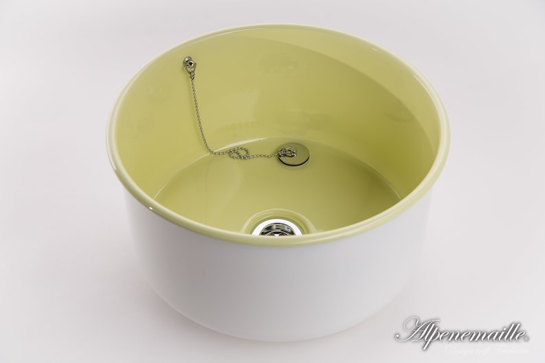 K&ouml;nnte beinhalten: Ein wei&szlig;es Keramikwaschbecken mit gelbem Innenraum. Das Waschbecken hat einen Abflussstopfen mit einer Kette.