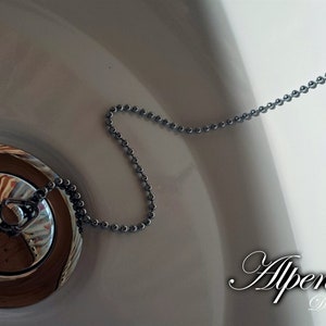May include: A close-up of a white porcelain sink with a chrome drain stopper and chain. The chain is attached to a small chrome knob at the top.