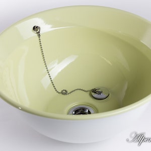 Puede incluir: Un lavabo de cer&aacute;mica verde claro con un borde blanco y un tap&oacute;n de desag&uuml;e cromado con una cadena.