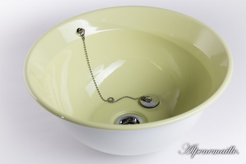Puede incluir: Un lavabo de cer&aacute;mica verde claro con un borde blanco y un tap&oacute;n de desag&uuml;e cromado con una cadena.