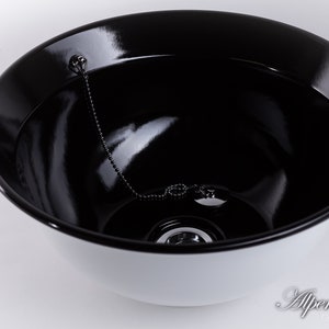 Puede incluir: Un cuenco de cer&aacute;mica blanca con un interior negro. El cuenco tiene una cadena y un tap&oacute;n de metal en el centro.