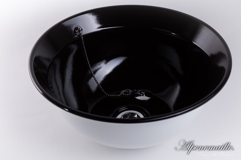 Puede incluir: Un cuenco de cer&aacute;mica blanca con un interior negro. El cuenco tiene una cadena y un tap&oacute;n de metal en el centro.