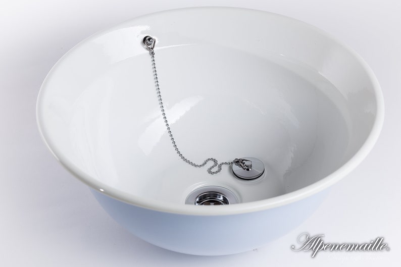 Puede incluir: Un lavabo de cer&aacute;mica blanca con un tap&oacute;n de desag&uuml;e cromado y una cadena. El lavabo est&aacute; vac&iacute;o y listo para usar.