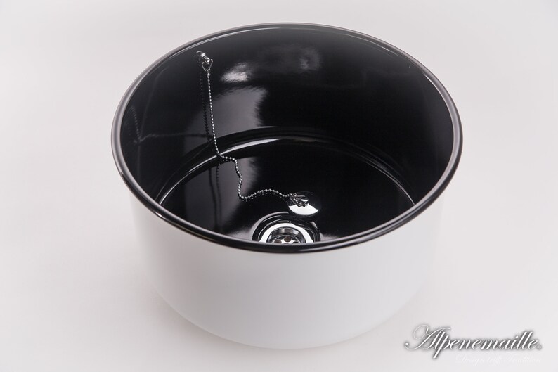 K&ouml;nnte beinhalten: Ein wei&szlig;es Keramiksp&uuml;lbecken mit schwarzem Innenraum. Das Sp&uuml;lbecken hat einen Abfluss mit einer Kette, die am Stopfen befestigt ist.