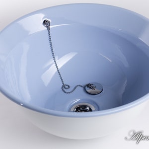Puede incluir: Un lavabo de cer&aacute;mica blanca con un interior azul claro. El lavabo tiene un tap&oacute;n de desag&uuml;e cromado con una cadena.