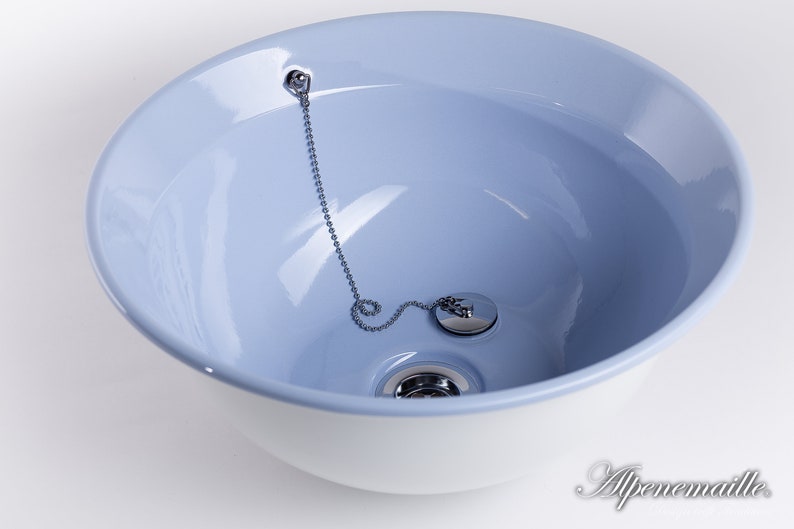 Puede incluir: Un lavabo de cer&aacute;mica blanca con un interior azul claro. El lavabo tiene un tap&oacute;n de desag&uuml;e cromado con una cadena.