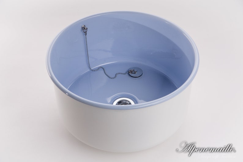 K&ouml;nnte beinhalten: Ein wei&szlig;es Keramikwaschbecken mit hellblauem Innenraum. Das Waschbecken hat einen Abfluss mit einer Kette und einem Stopfen.