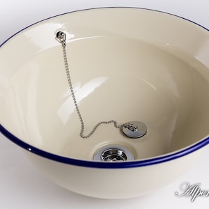 Puede incluir: Un lavabo de cer&aacute;mica blanca con un borde azul y un tap&oacute;n de desag&uuml;e cromado con una cadena.