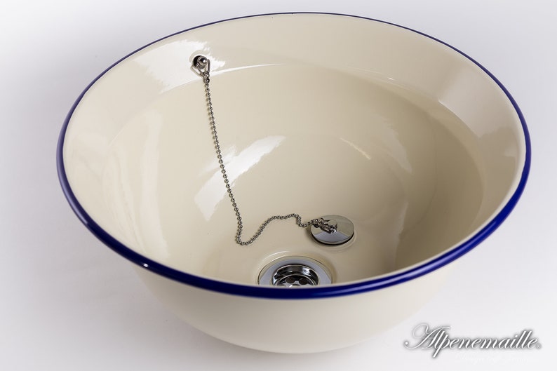 Puede incluir: Un lavabo de cer&aacute;mica blanca con un borde azul y un tap&oacute;n de desag&uuml;e cromado con una cadena.