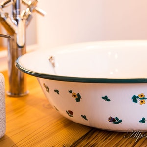 May include: A white enamel sink with a green rim and a floral pattern. The sink is on a wooden countertop.