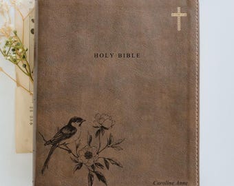 May include: Brown leather Holy Bible with a debossed bird and floral design. The cover features the words "HOLY BIBLE" and a cross. The name "Caroline Anne" is printed at the bottom.