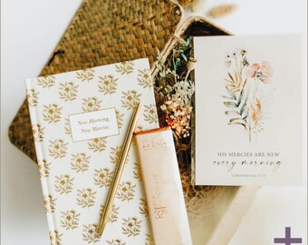 May include: A gift basket containing a white journal with a gold floral pattern, a gold pen, a chocolate bar, and a card with a floral design and the text "His mercies are new every morning, Lamentations 3:23".