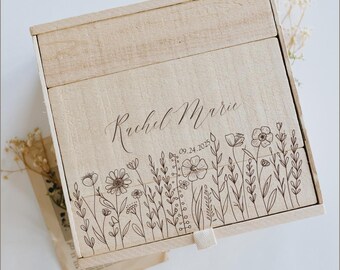 May include: A light-coloured wooden box with a sliding lid. The box is engraved with the name "Rachel Marie" in cursive script and the date "09.24.2025". A floral design borders the bottom edge of the box.