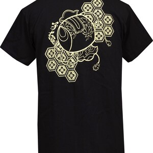 Peut inclure: T-shirt noir avec un imprim&eacute; graphique dor&eacute; repr&eacute;sentant un poisson japonais stylis&eacute; avec des motifs g&eacute;om&eacute;triques et le texte "魚" au dos.