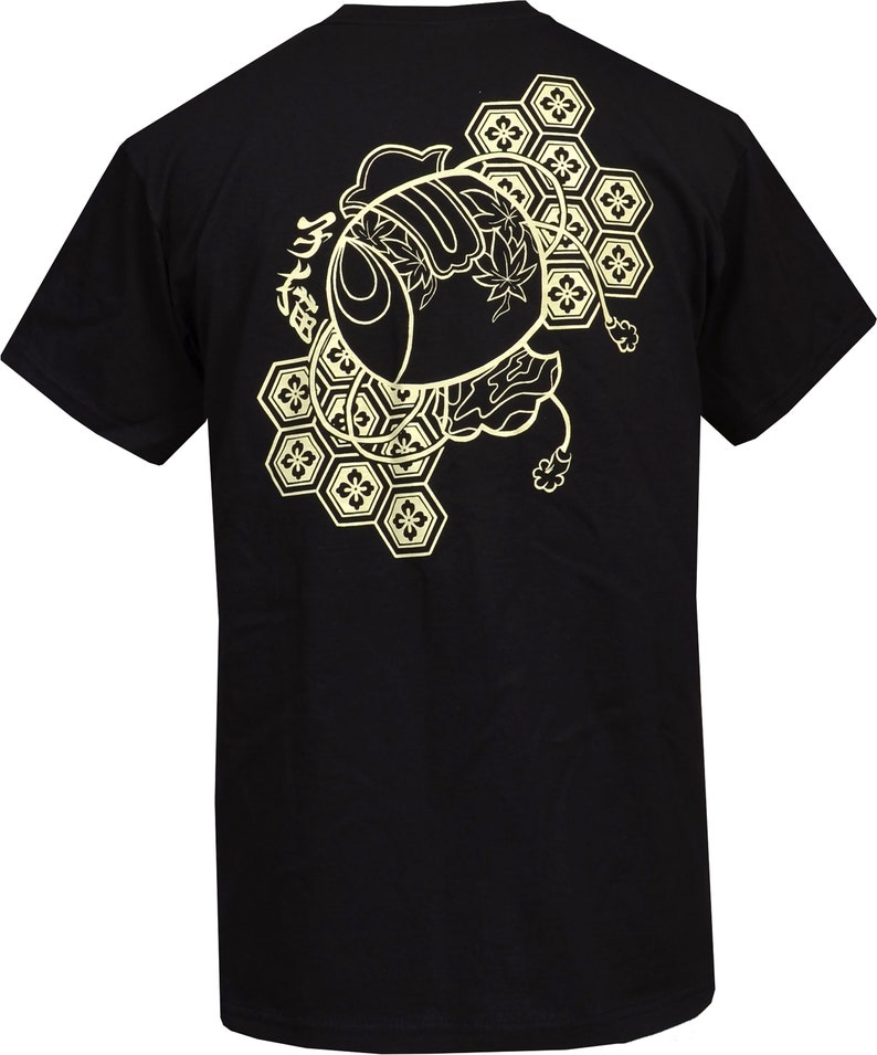 Peut inclure: T-shirt noir avec un imprim&eacute; graphique dor&eacute; repr&eacute;sentant un poisson japonais stylis&eacute; avec des motifs g&eacute;om&eacute;triques et le texte "魚" au dos.