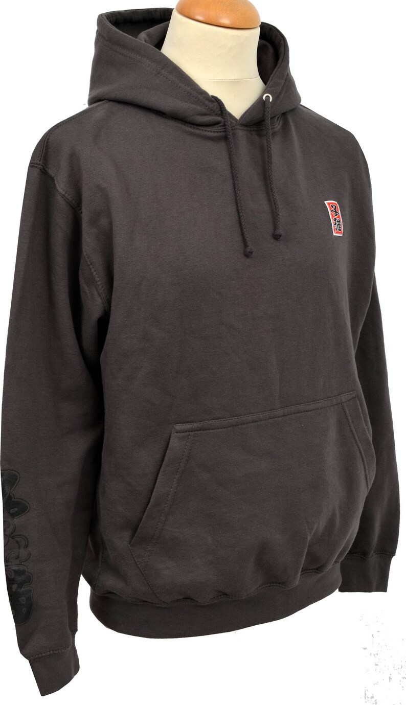 May include: A dark gray hooded sweatshirt with a small red and black logo on the right chest and a larger black logo on the left sleeve. The hoodie has a drawstring hood and a kangaroo pocket.