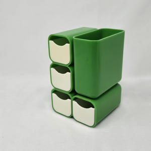 May include: A set of green plastic storage containers. The containers are rectangular with rounded corners. Four of the containers have a white interior. The containers are stacked together, with one container on top and the other four arranged below.