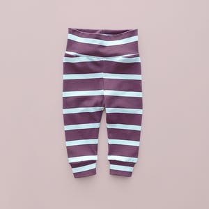 Puede incluir: Pantalones de bebé a rayas moradas y azul claro. Los pantalones tienen una cintura alta y están hechos de un material suave. Las rayas son horizontales y espaciadas uniformemente. Los pantalones están diseñados para la comodidad y el estilo.