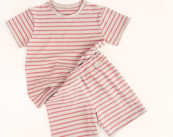 May include: A short-sleeved crew neck t-shirt and matching shorts set featuring a horizontal striped pattern in muted red and off-white. The shorts have an elasticized waistband, and both pieces are made of a soft, lightweight fabric.
