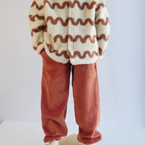 May include: A cream-coloured sherpa fleece jacket featuring a brown wavy line pattern and a front zip closure, paired with solid rust-coloured corduroy trousers that have a straight-leg fit and a textured ribbed surface throughout.