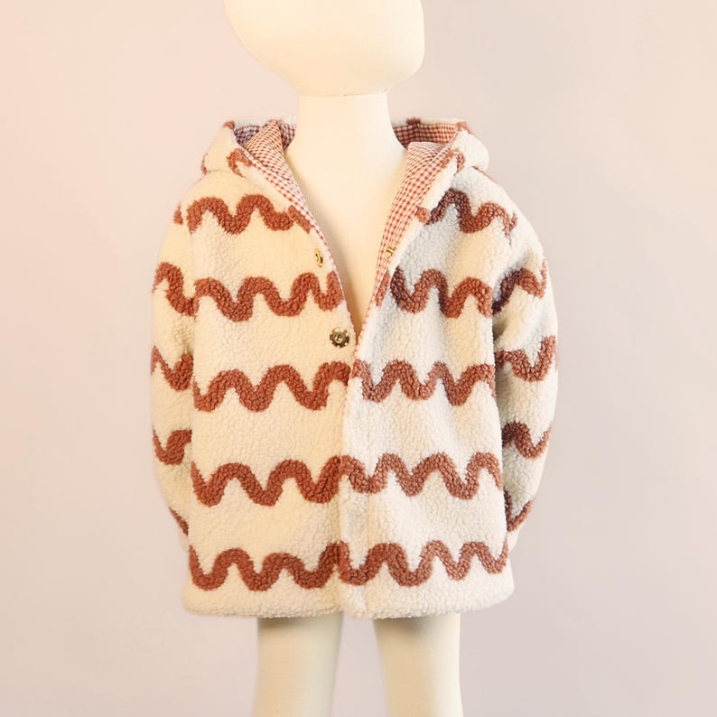 Puede incluir: Chaqueta con capucha de color crema con un patr&oacute;n ondulado de color &oacute;xido. La chaqueta tiene cierre de botones y un forro de cuadros rojos y blancos en la capucha. La chaqueta se muestra en un maniqu&iacute;.