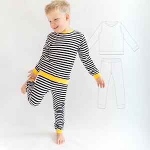 Puede incluir: Un conjunto de camiseta de manga larga y pantalón con un patrón de rayas horizontales en blanco y negro, con ribetes amarillos sólidos en el cuello, los puños y la cintura. A la derecha se muestra un dibujo técnico del conjunto.