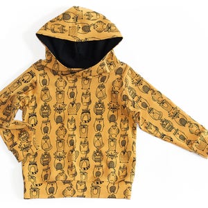 May include: A mustard yellow hooded sweatshirt with a black and white print of various woodland animals. The animals include owls, raccoons, foxes, and deer.