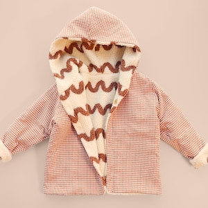 Puede incluir: Chaqueta con capucha para ni&ntilde;os con un estampado de cuadros rojos y blancos en el exterior. El interior es de material crema y esponjoso con dise&ntilde;os ondulados marrones. La chaqueta tiene cierre de bot&oacute;n y pu&ntilde;os esponjosos.