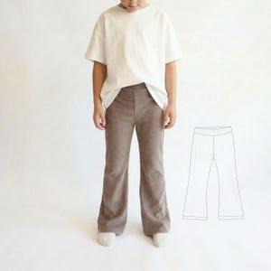 Puede incluir: Un niño con una camiseta blanca y pantalones de pana marrones. Los pantalones tienen un diseño de pierna acampanada. Un dibujo lineal de los pantalones se muestra a la derecha. El fondo es blanco.